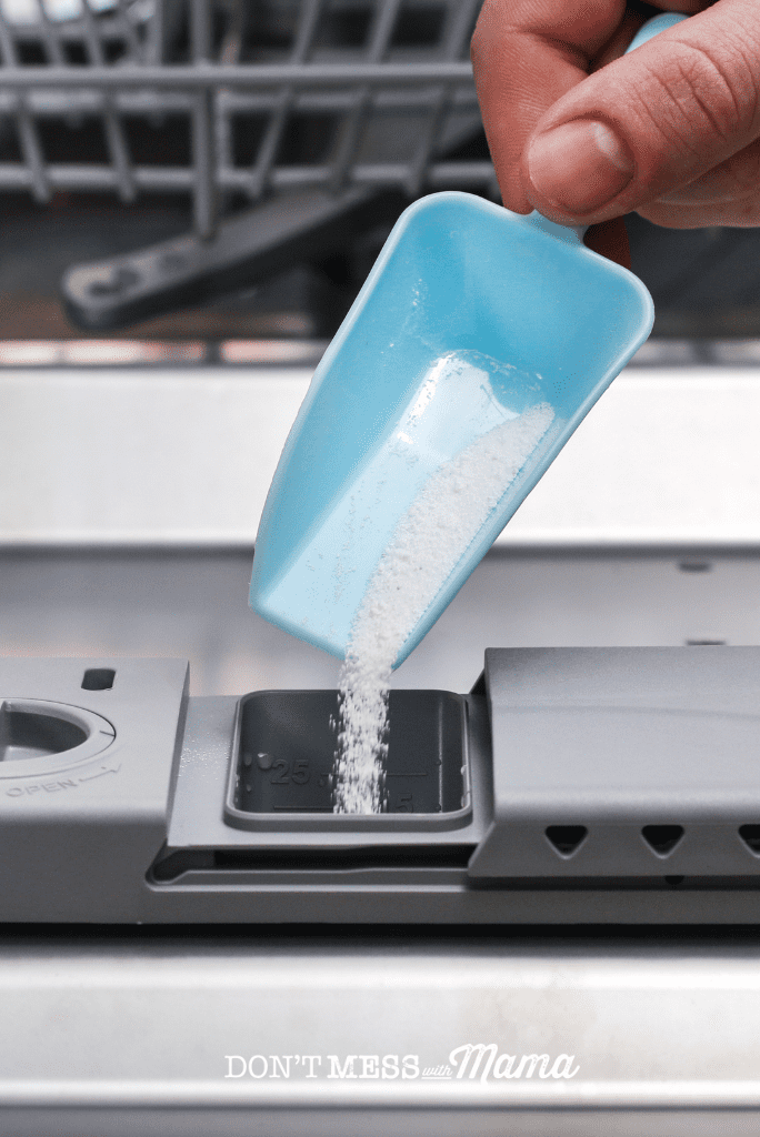 blue scoop adding homemade dishwasher rinse aid to compartment