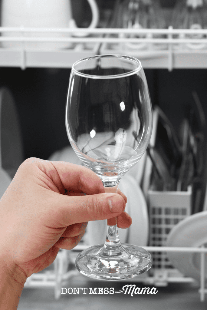 hand holding sparkling clean glass with dishwasher in background