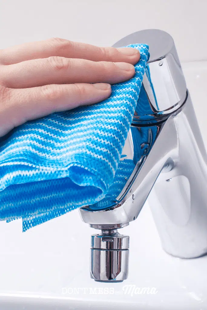 hand using blue cloth to clean faucet
