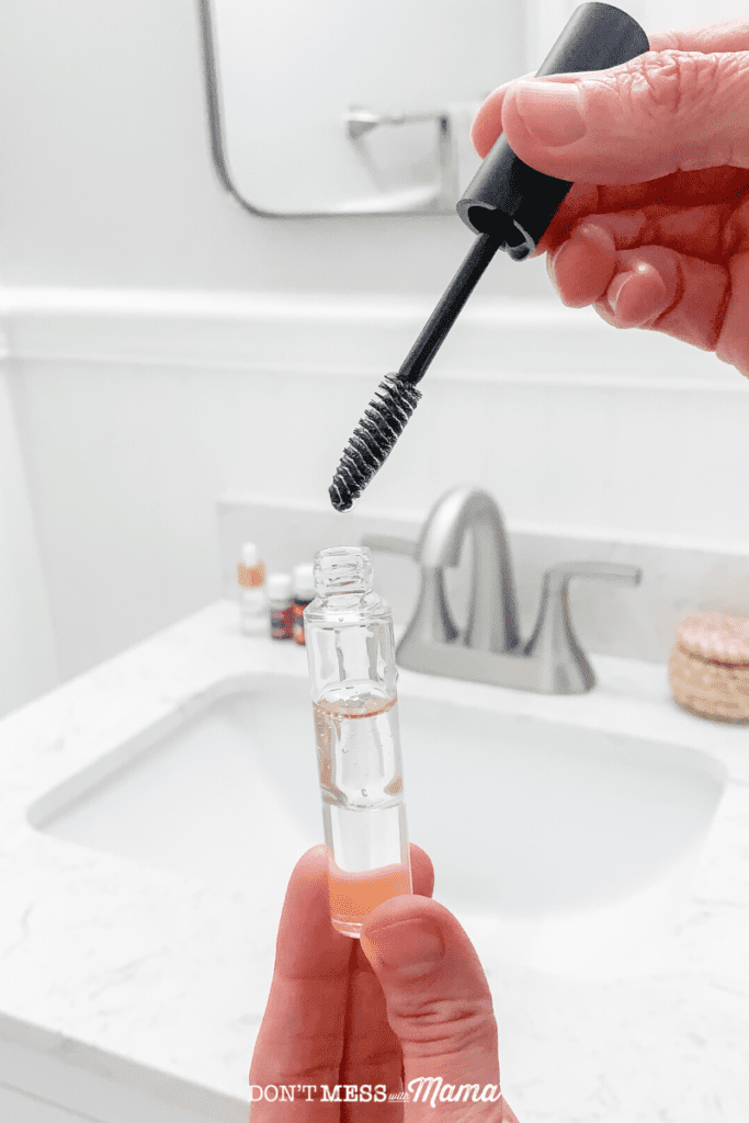 hands holding mascara tube with eyelash growth serum above sink