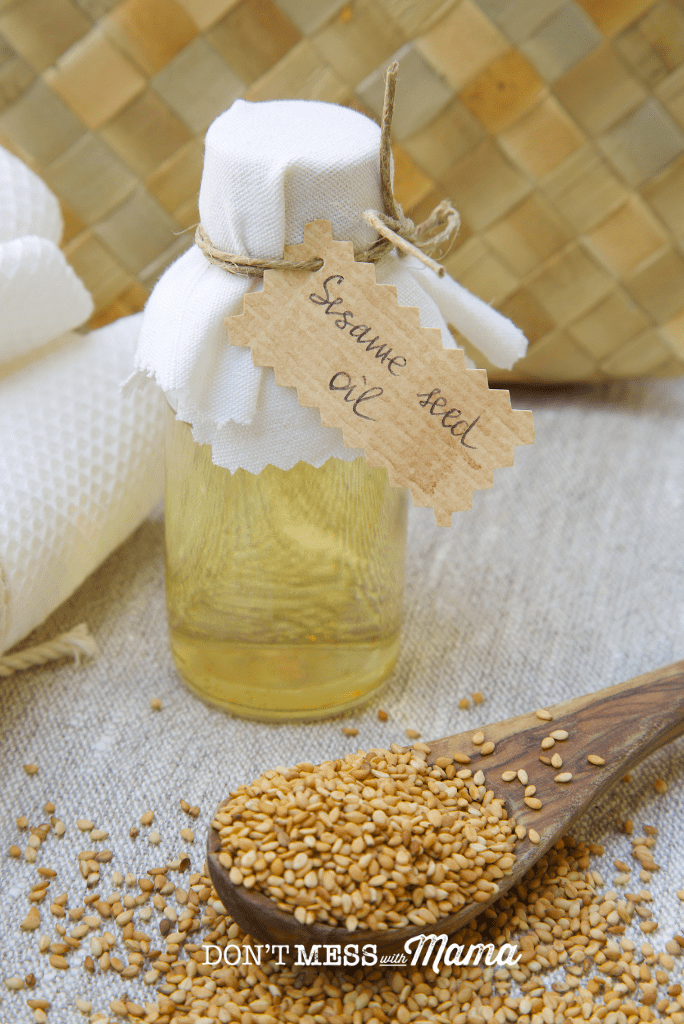 glass bottle of sesame seed oil with spoonful of seeds