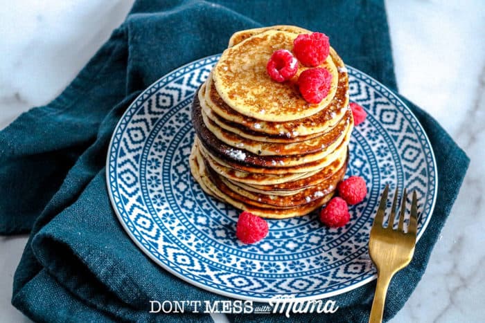 stack of low carb pancakes ona blue printed plate topped with raspberries