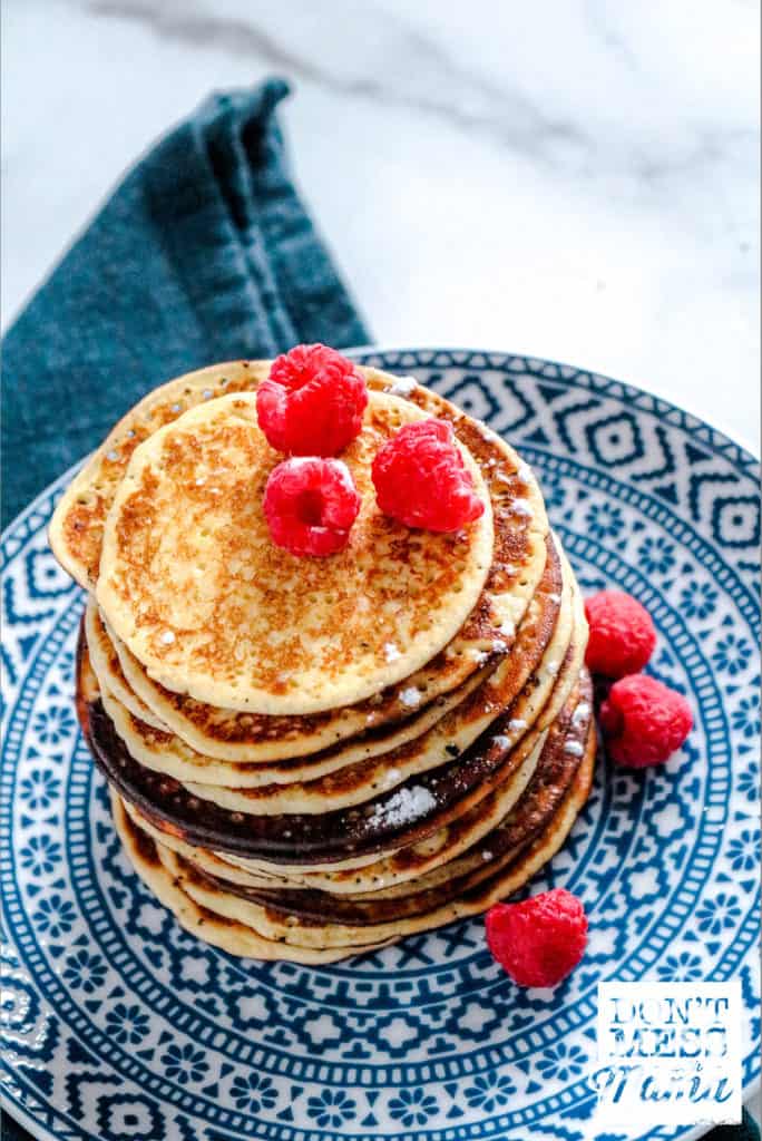 stack of low carb pancakes on blue printed plate topped with raspberries