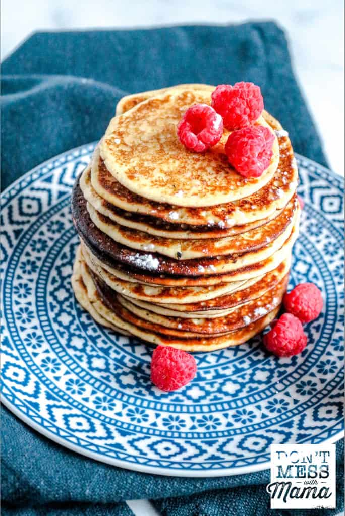 stack of low carb pancakes on blue printed plate topped with raspberries