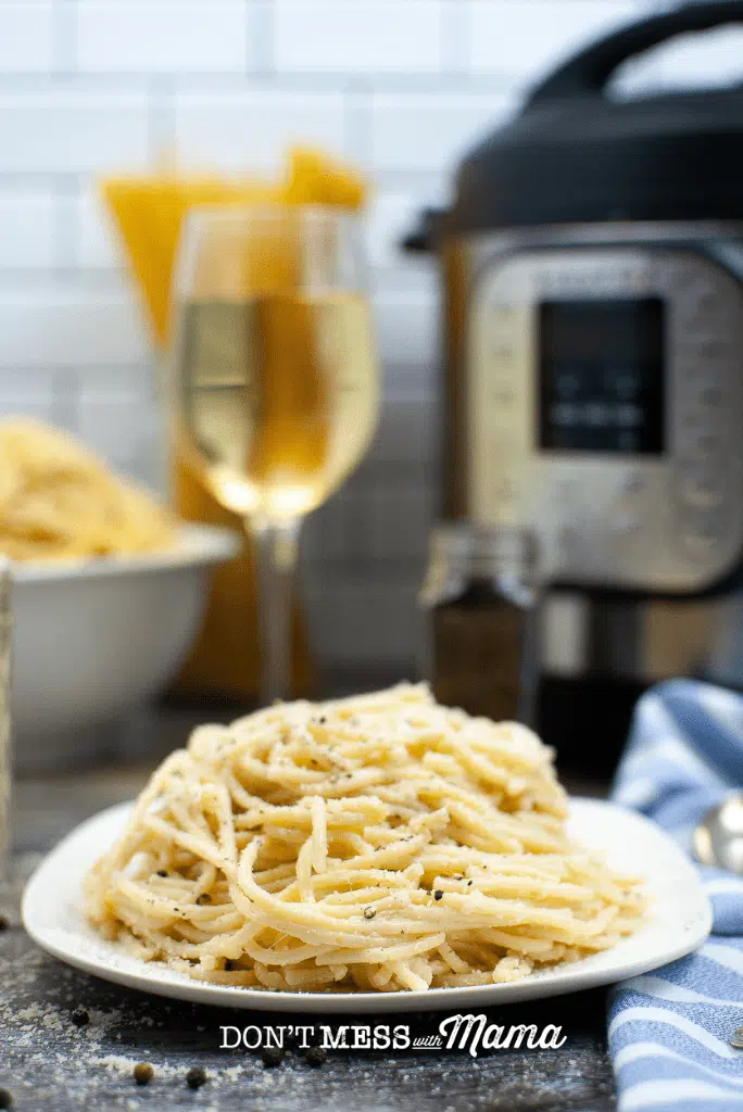 white plate with spaghetti cacio e pepe and glass of white wine and instant pot in background