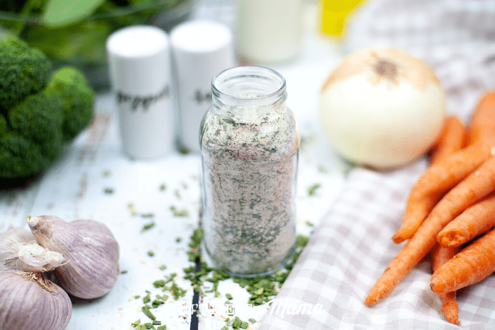 small glass bottle of dry ranch seasoning mix with carrots, onion and garlic in background