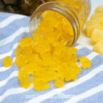 glass jar with pineapple gummy bears overflowing onto blue striped cloth