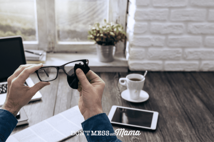 man cleaning glasses with coffee on desk in background