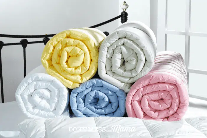 yellow, white, green, blue and pink blankets rolled up on bed