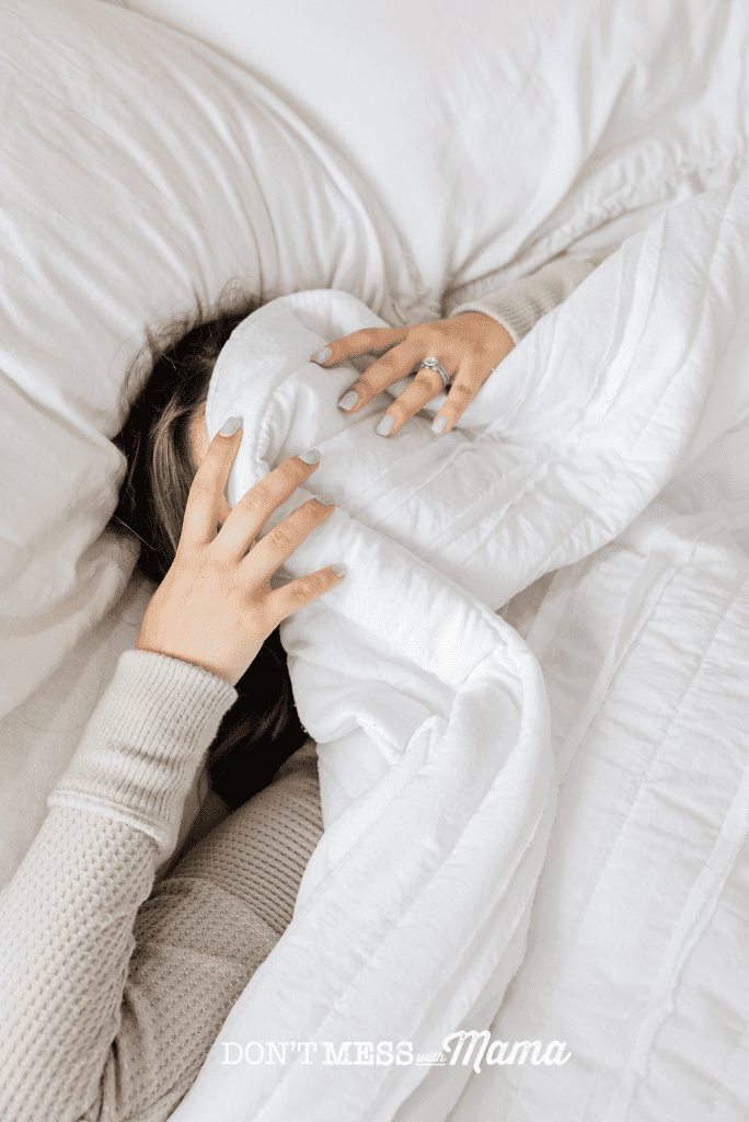woman in white bed sheets with hands over face