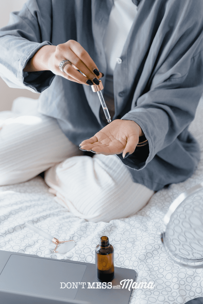 woman in blue cardigan pouring jojoba oil onto hand