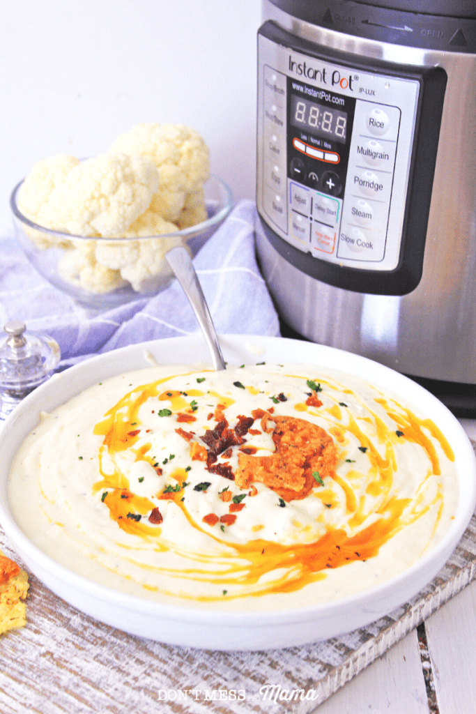 closeup of cauliflower soup in a white bowl on a table with an Instant Pot in the background