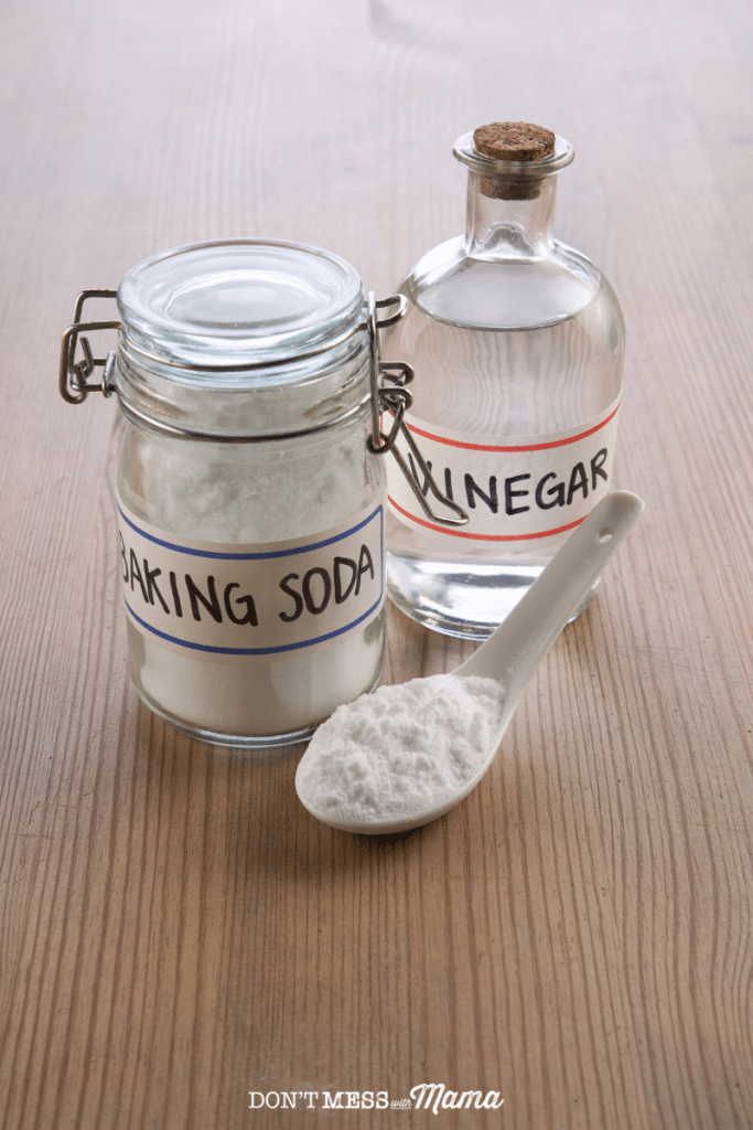 baking soda and vinegar on glass jars on a table with a spoonful of baking soda nearby