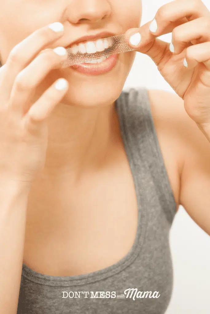 woman in grey vest applying tooth whitening strips