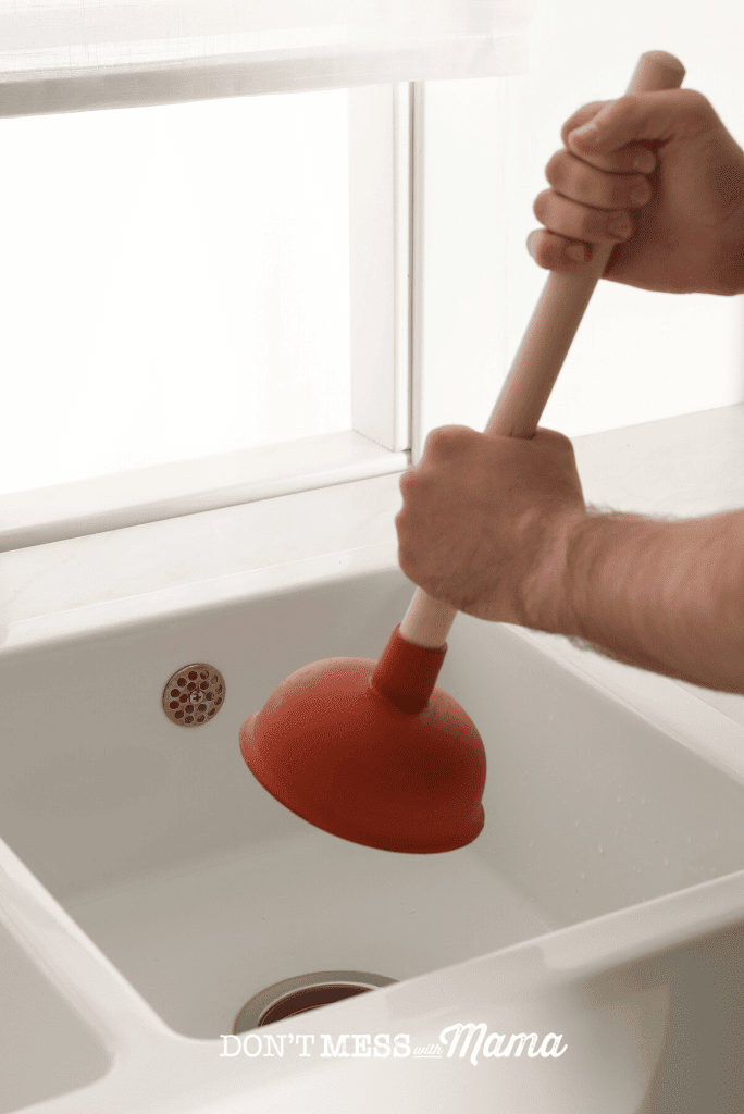 hand holding red plunger in sink