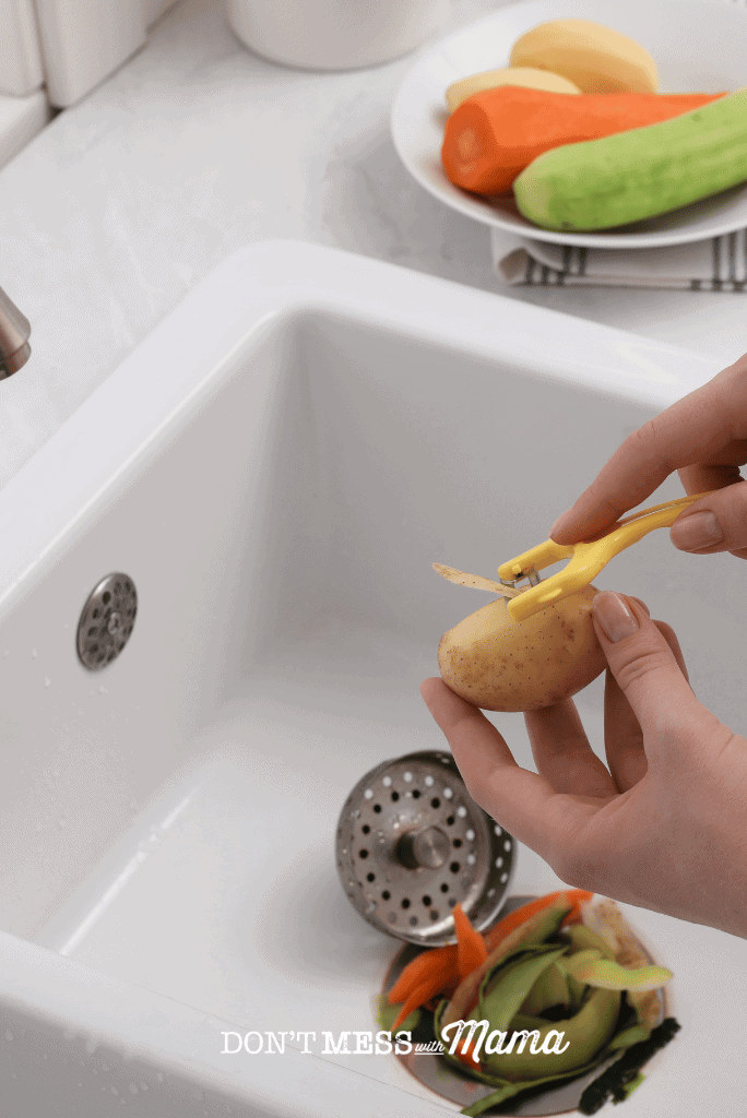 hand peeling potato into garbage disposal