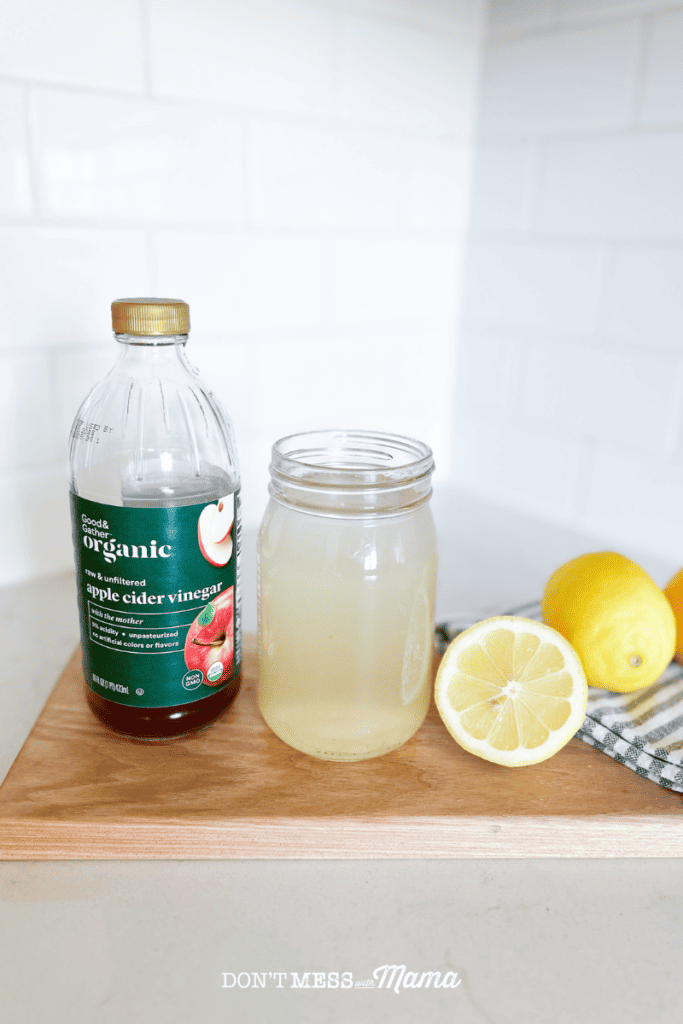apple cider vinegar and lemon juice drink on a cutting board with lemons and a bottle of viengar nearby