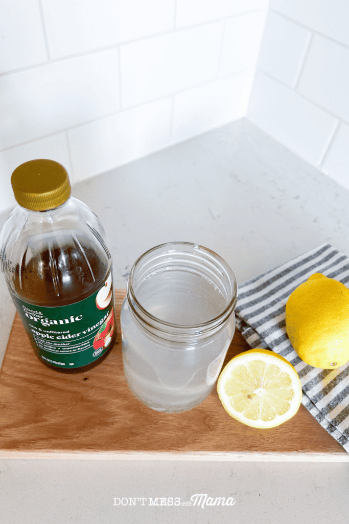 closeup shot of lemon juice in a glass of water with a bottle of apple cider vinegar and lemons sitting on a cutting board 