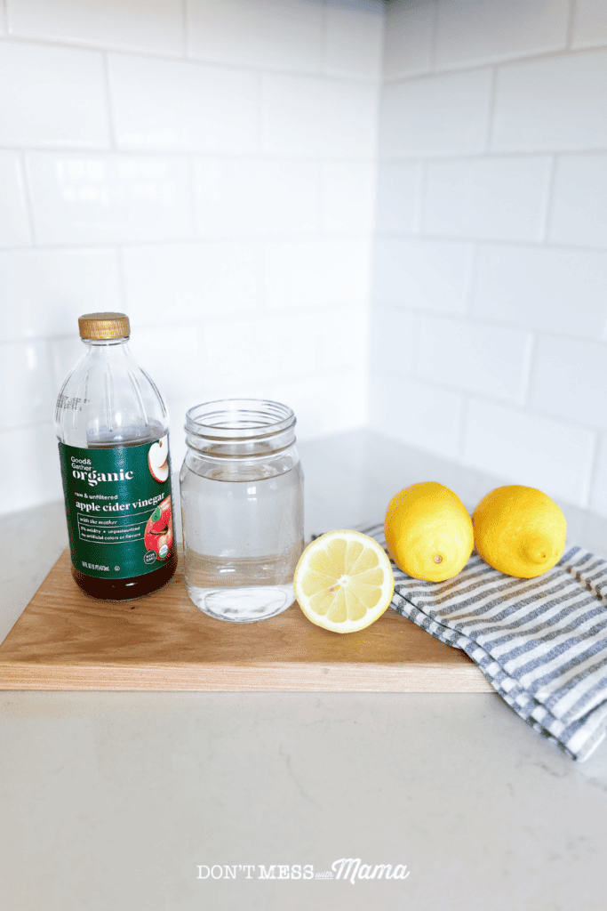 a bottle of apple cider vinegar and lemons sitting on a cutting board on. a kitchen counter with a glass of water