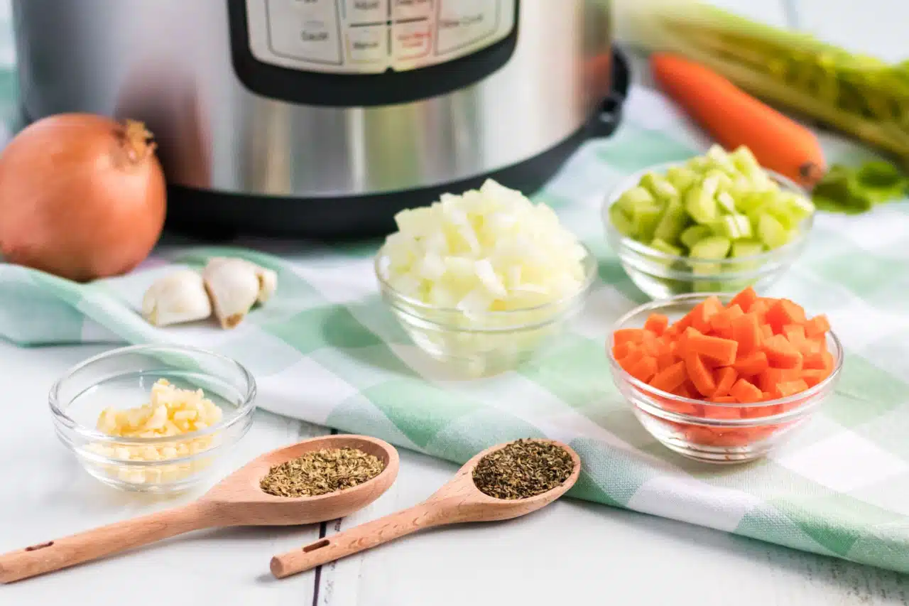 chopped oninos, carrots, celery in small bowls next to spoons with herbs next to an Instant Pot