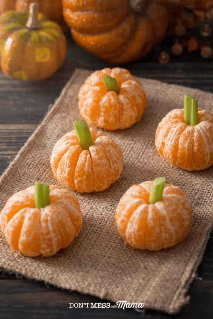 closeup of small oranges peeled with celery sticks in the middle to look like mini pumpkins