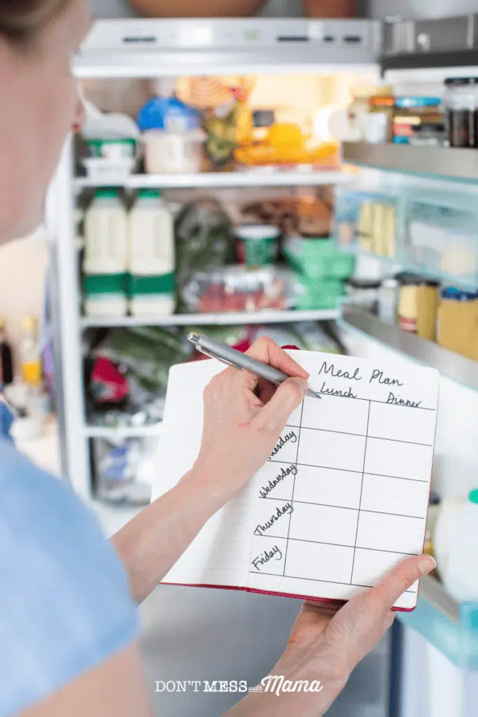 woman in front of an open refrigerator with a notepad and pen to make meal plan