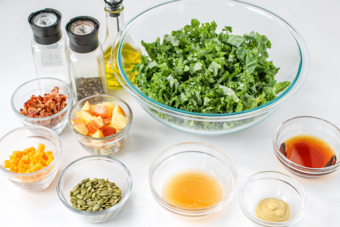 ingredients to make a kale salad with apples, cheddar, and bacon in clear glass containers