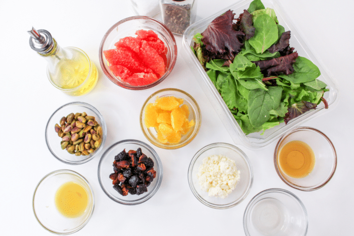 ingredients to make a summer citrus salad like salad greens, pistachios, dried figs, and feta cheese